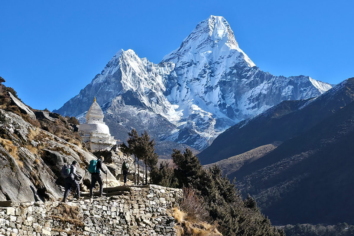 Trekkers walking past a stupa with Mount Ama Dablam in the background.⁠
